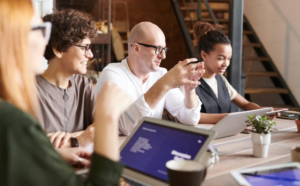 Team of professionals in a meeting discussing ideas around a table with laptops and tablets in a modern office